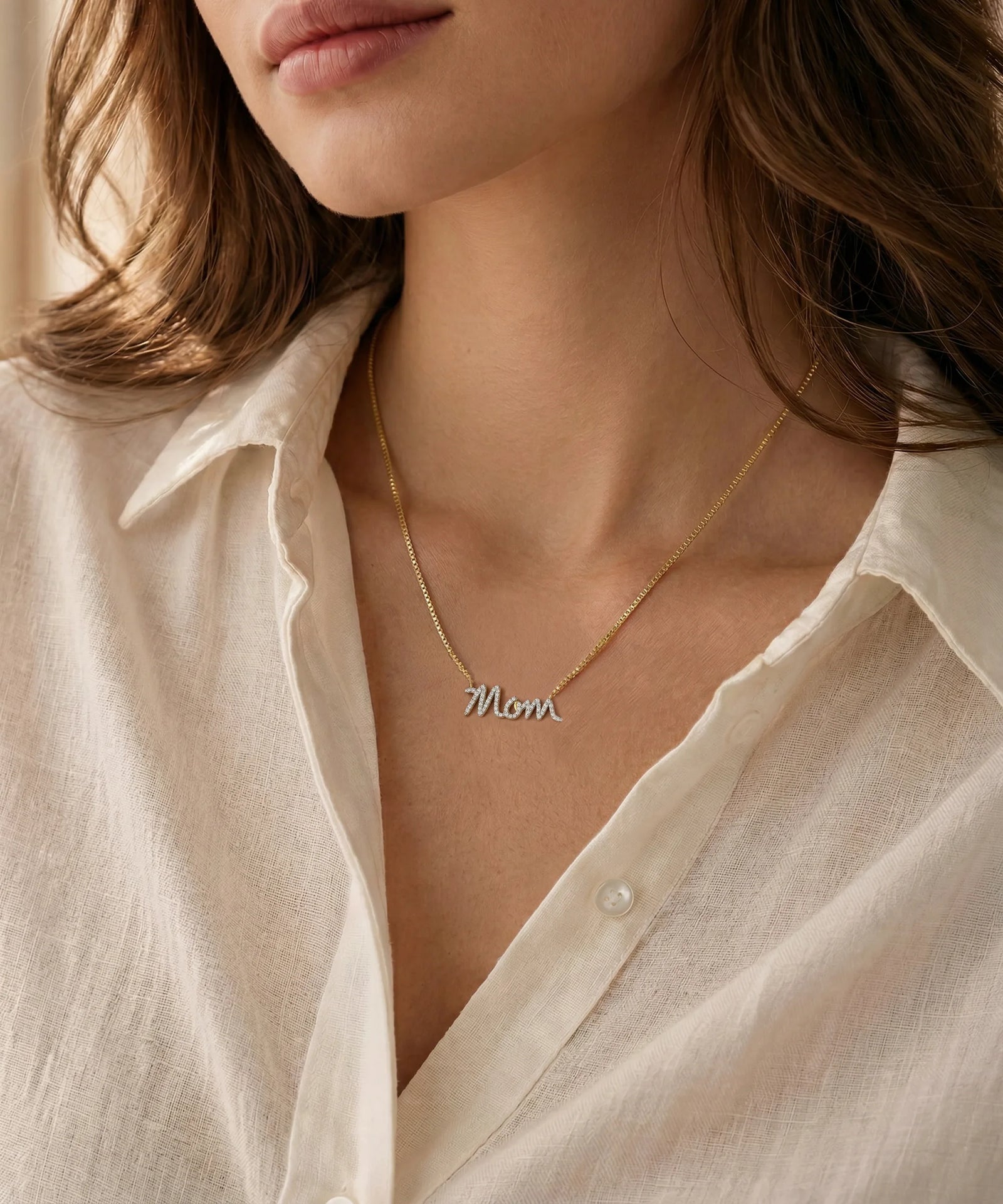 Close-up of a person wearing a delicate gold necklace with an oval pendant against a neutral background.