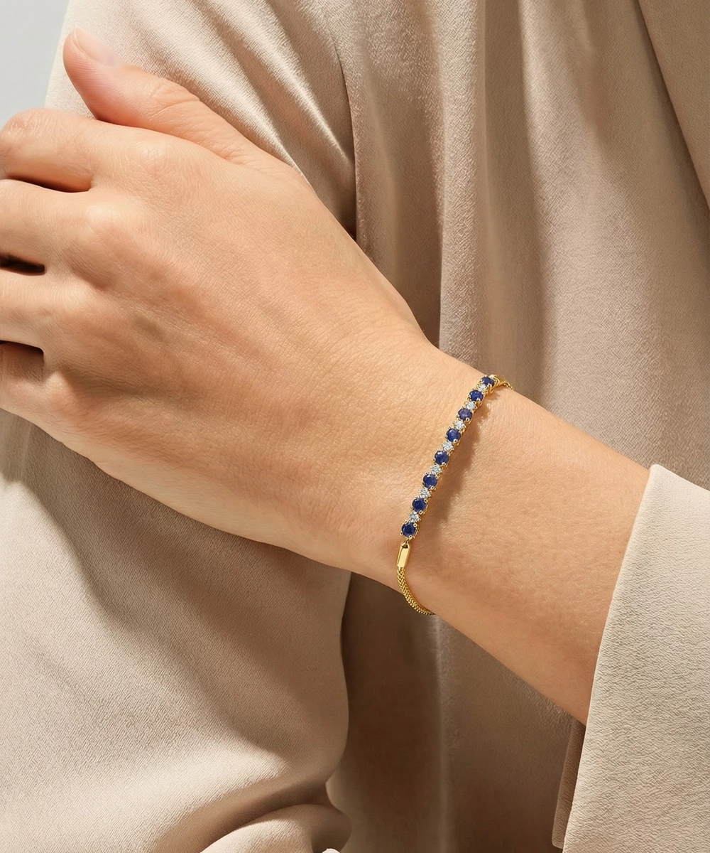 Gold bracelet with blue beads on a wrist against a beige background