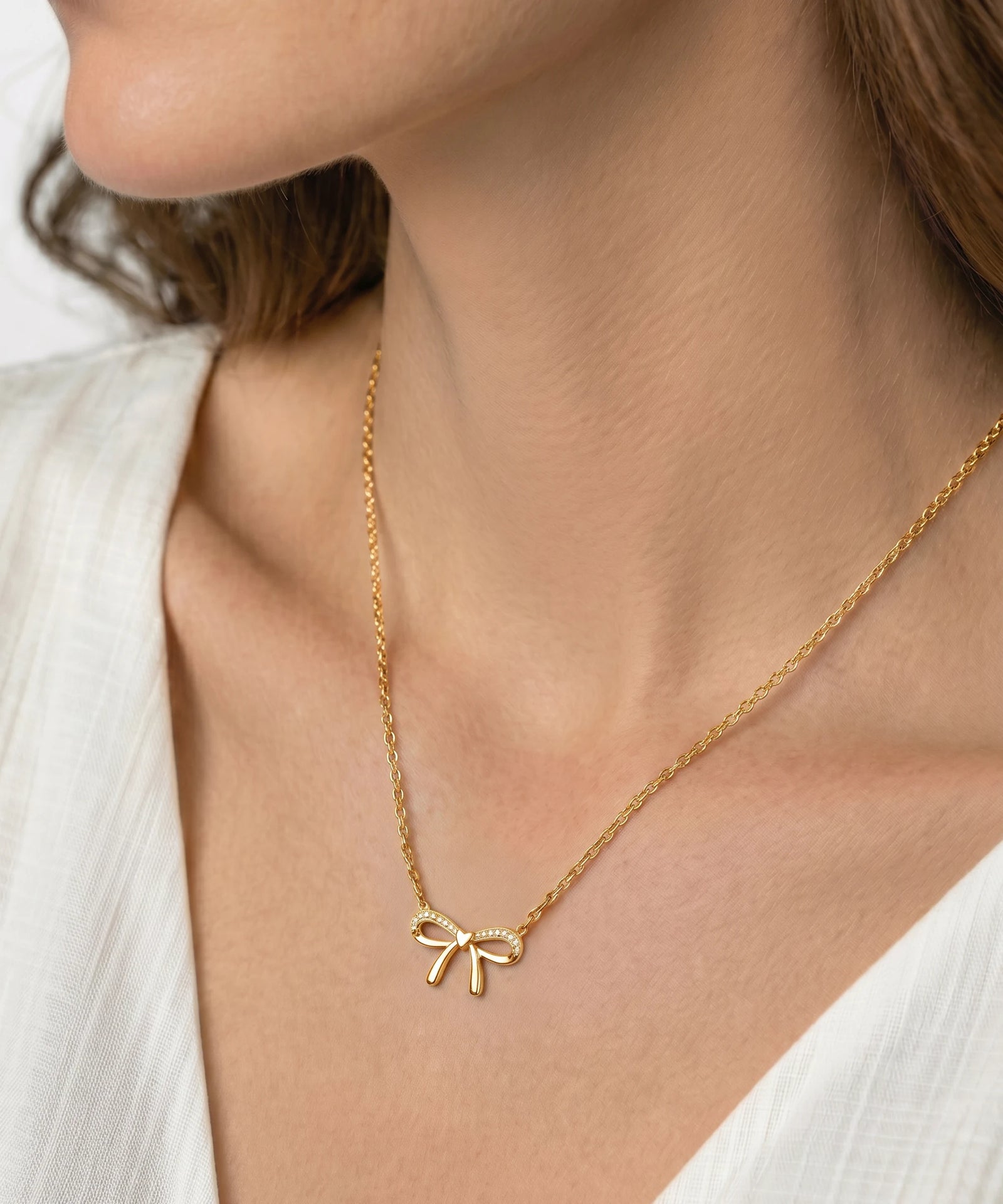 Gold necklace with a bow pendant worn by a person against a neutral background