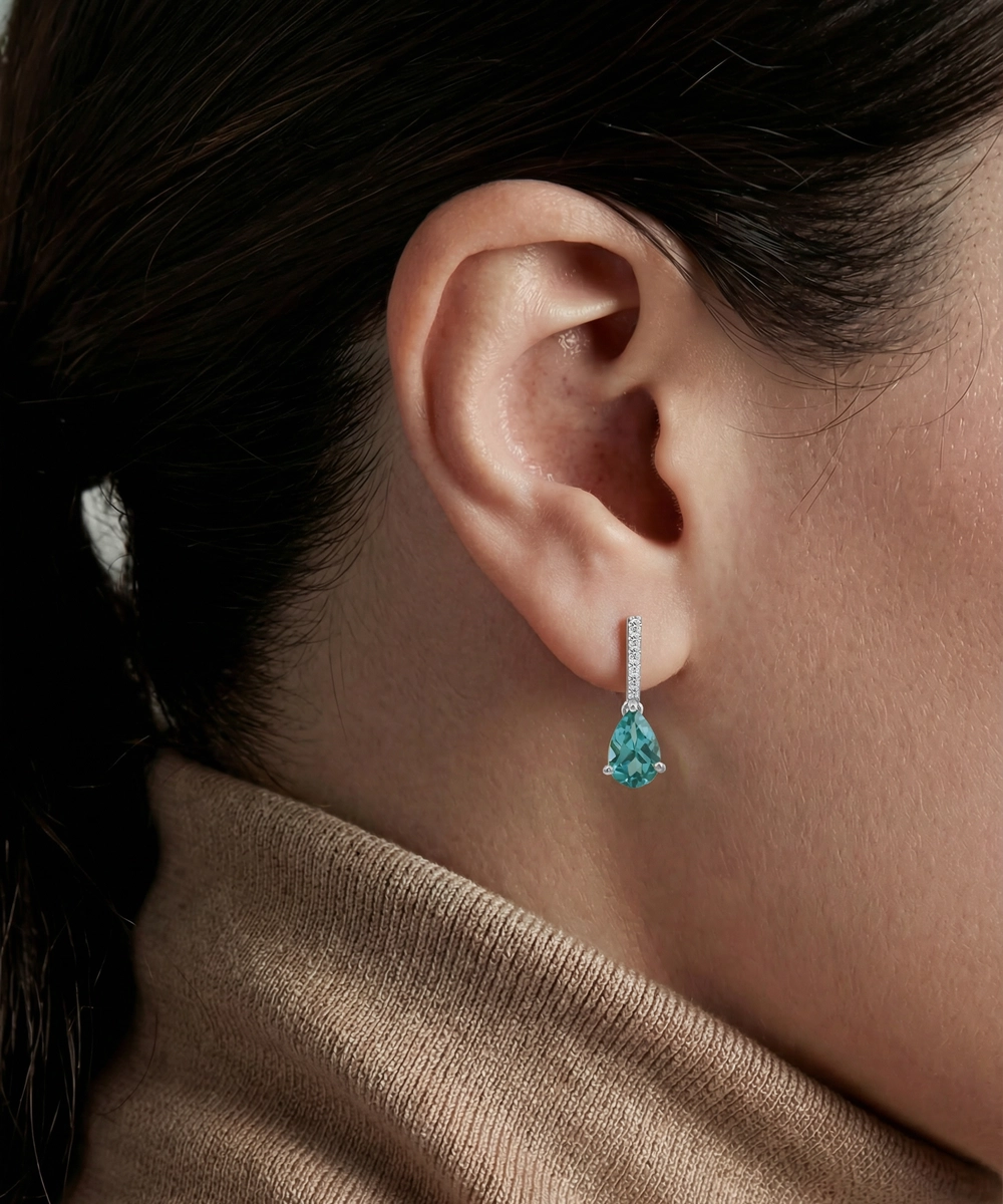 Close-up of a person wearing turquoise teardrop earrings with a neutral background