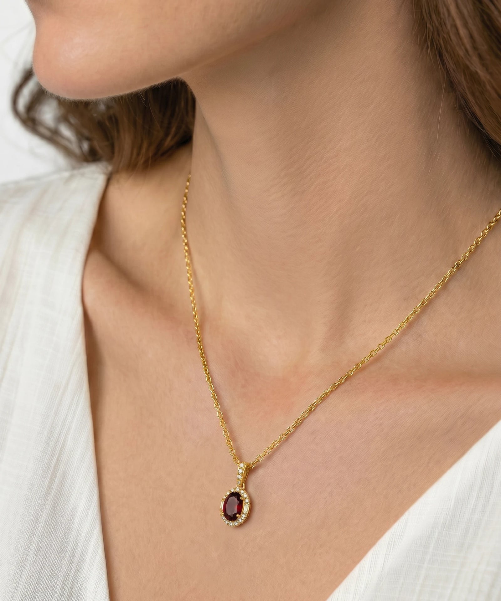 Gold necklace with a red gemstone pendant worn by a person in a white outfit.