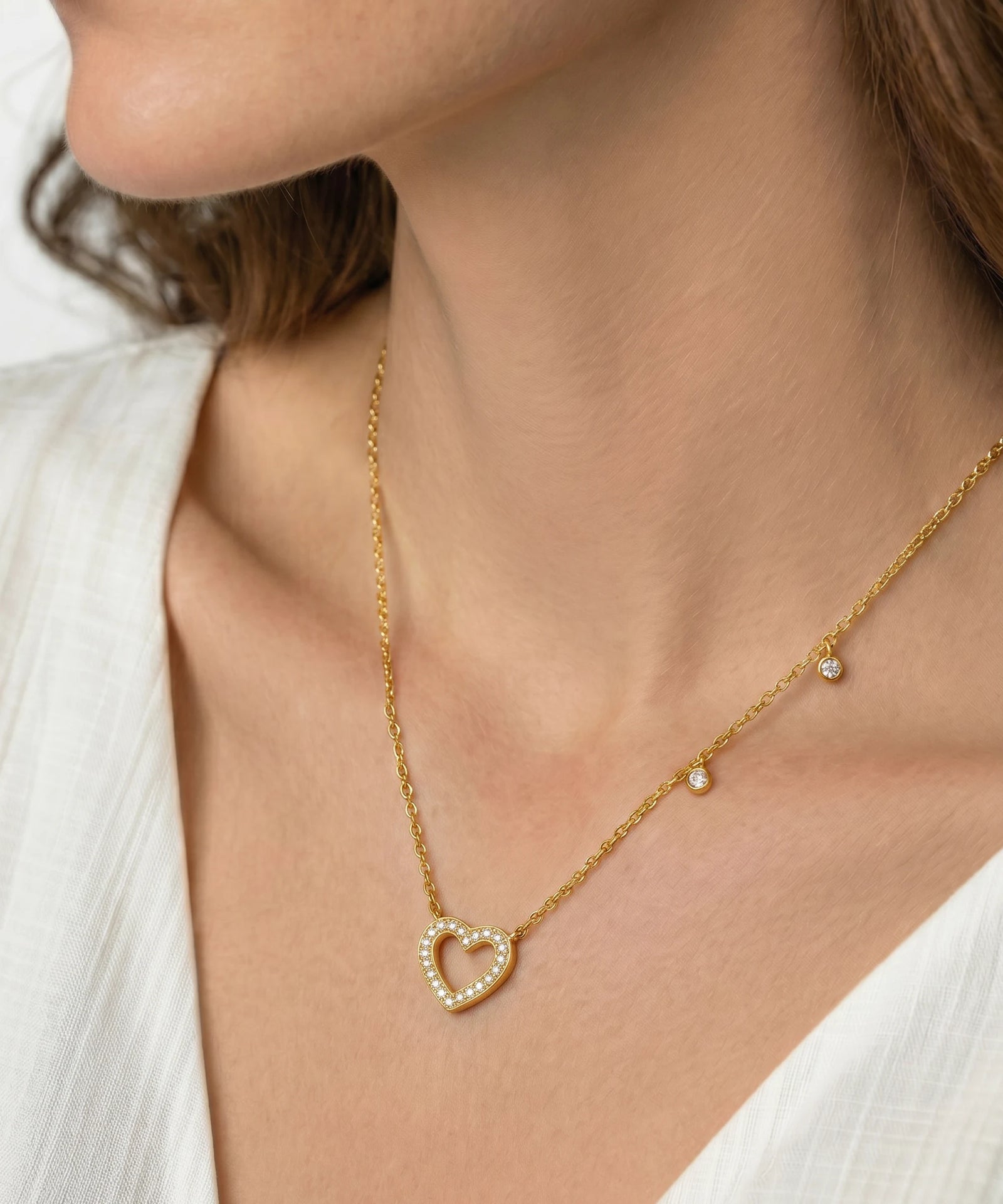 Gold necklace with a heart-shaped pendant worn by a person in a white outfit.