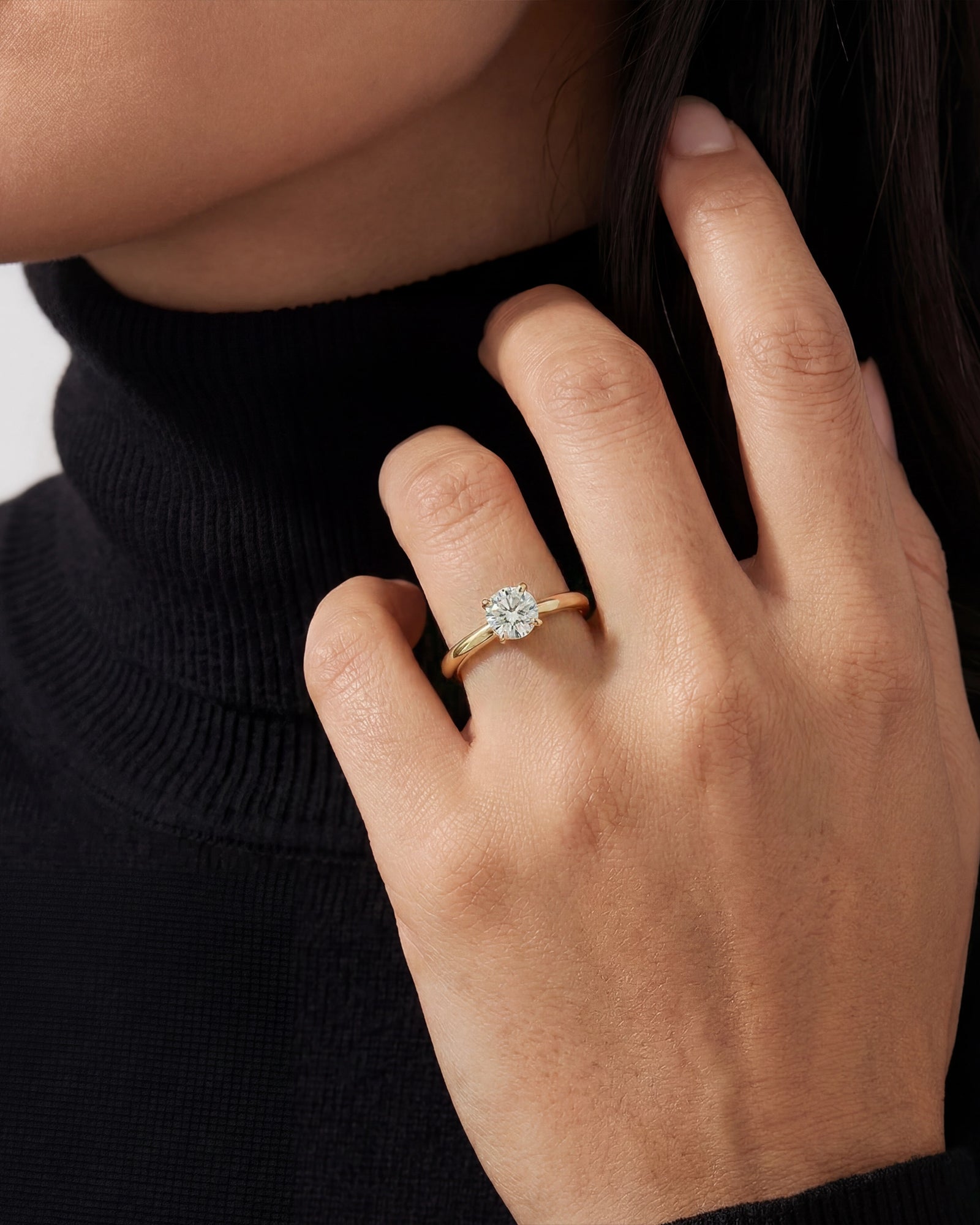 Close-up of a hand wearing a gold ring with a diamond on a plain background