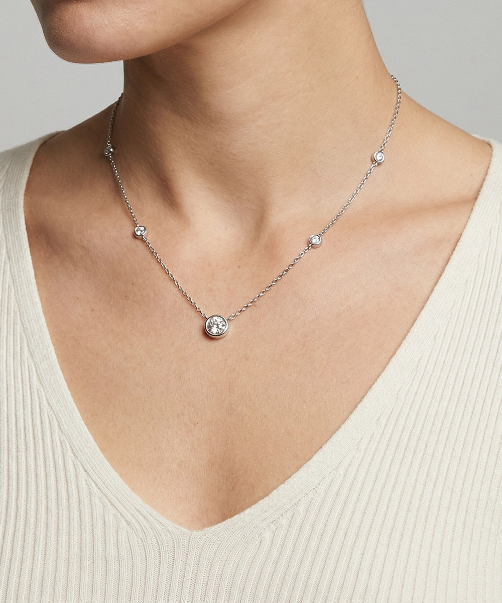Necklace with a round pendant on a person wearing a beige top against a neutral background