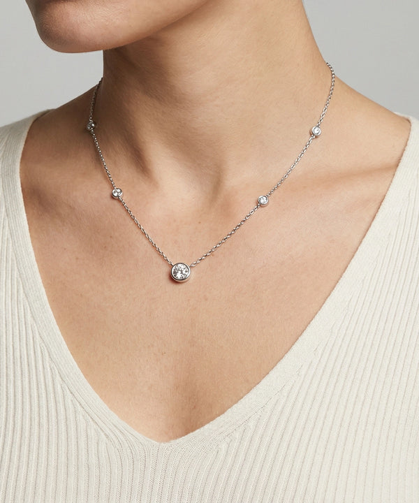 Necklace with a round pendant on a person wearing a beige top against a neutral background