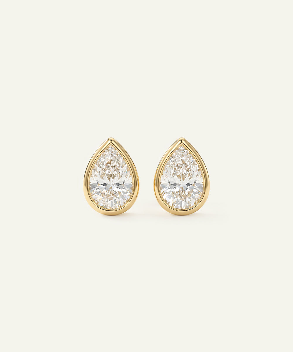 Gold teardrop earrings with clear gemstones on a light beige background