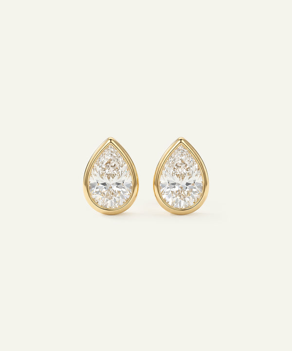 Gold teardrop earrings with clear gemstones on a light beige background