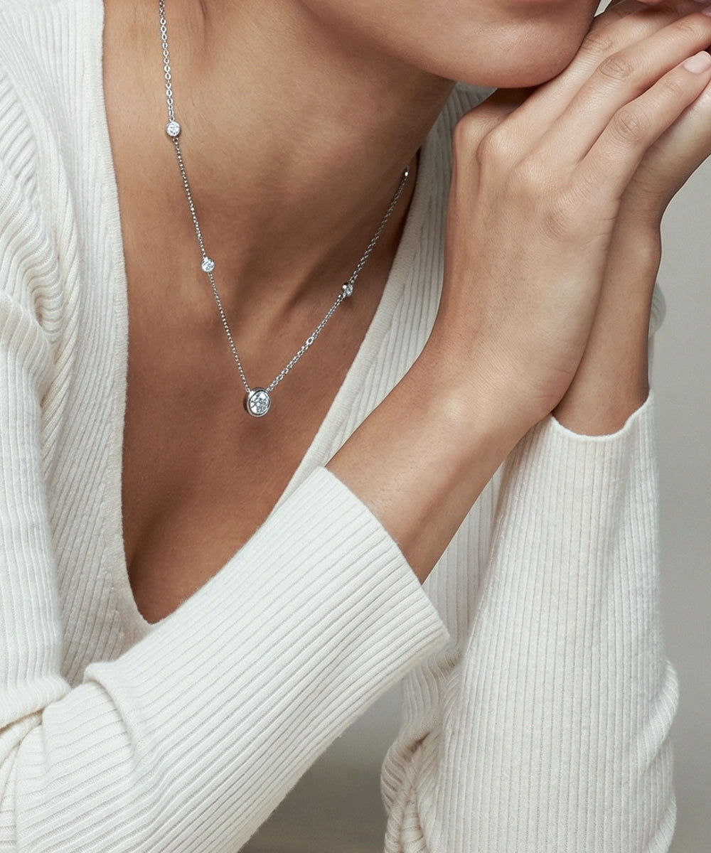 Silver necklace with a pendant worn by a person in a white sweater.