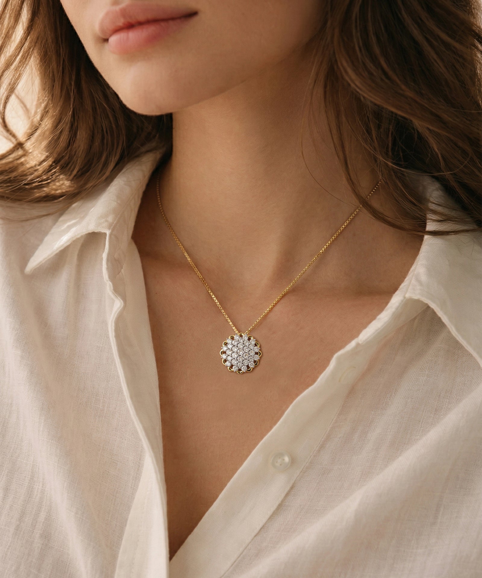 Close-up of a silver necklace with a floral pendant worn by a person in a light-colored shirt.