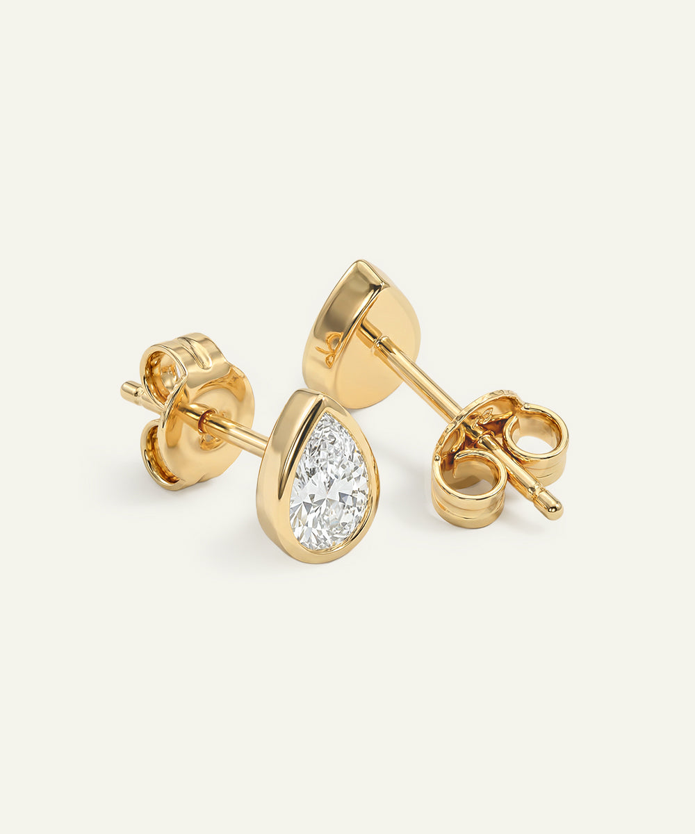 Gold teardrop-shaped stud earrings with clear gemstones on a light beige background