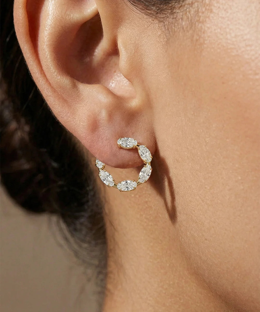 Close-up of a person wearing a diamond hoop earring with a neutral background