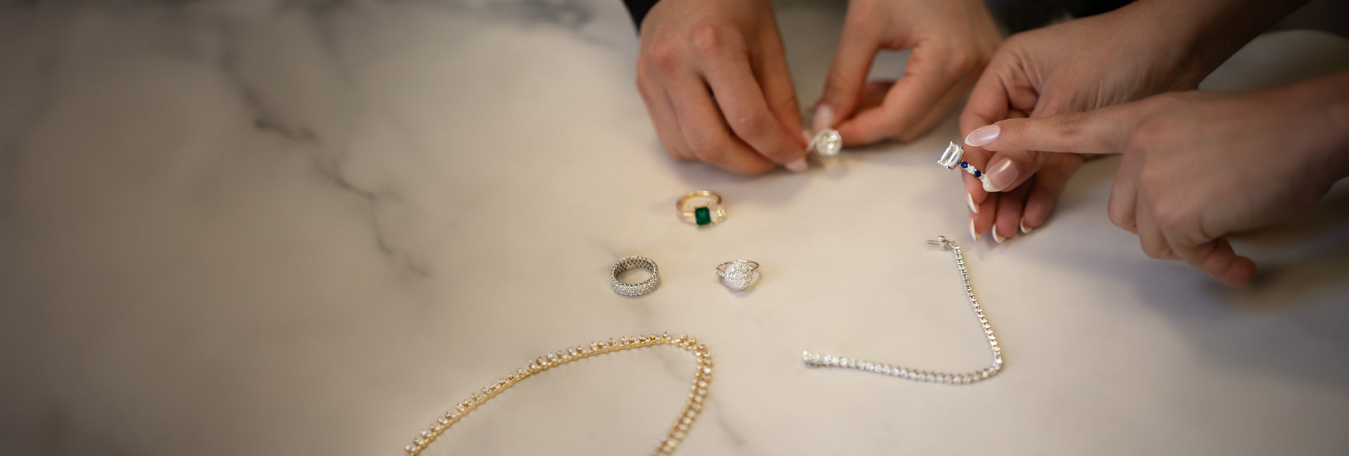 Hands arranging jewelry on a marble surface