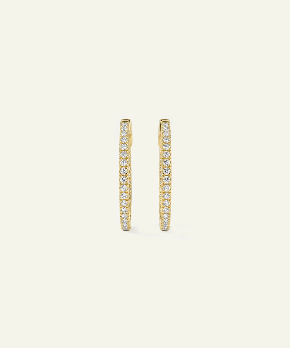 Gold hoop earrings with embedded stones on a light beige background