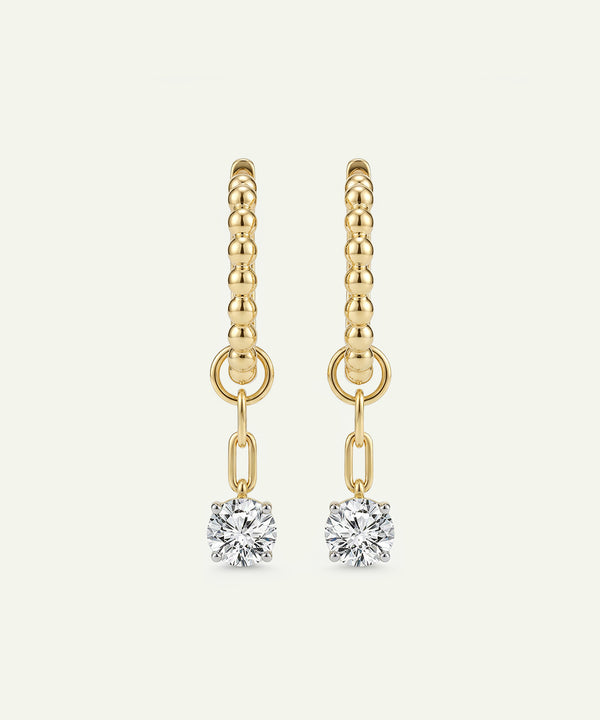 Gold earrings with diamond drops on a light beige background