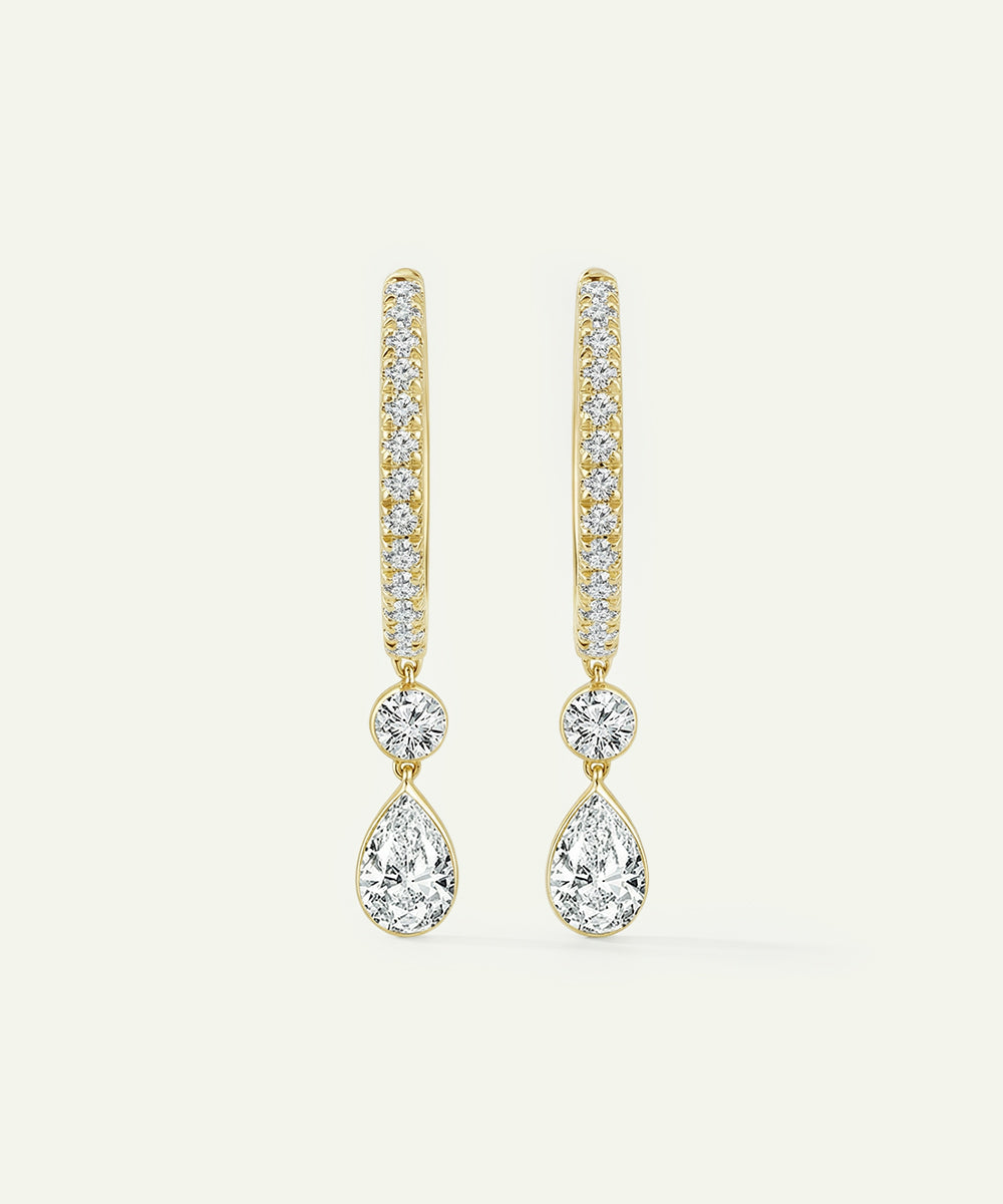 Gold teardrop earrings with clear gemstones on a light beige background