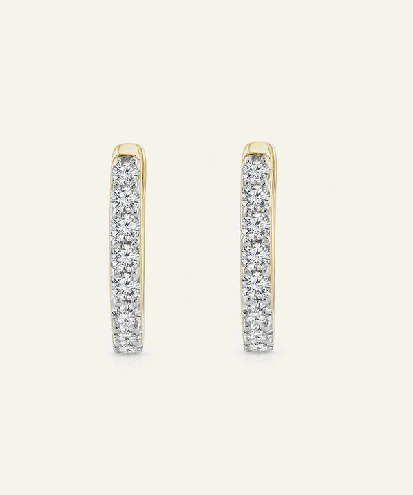 Gold hoop earrings with clear gemstones on a light beige background
