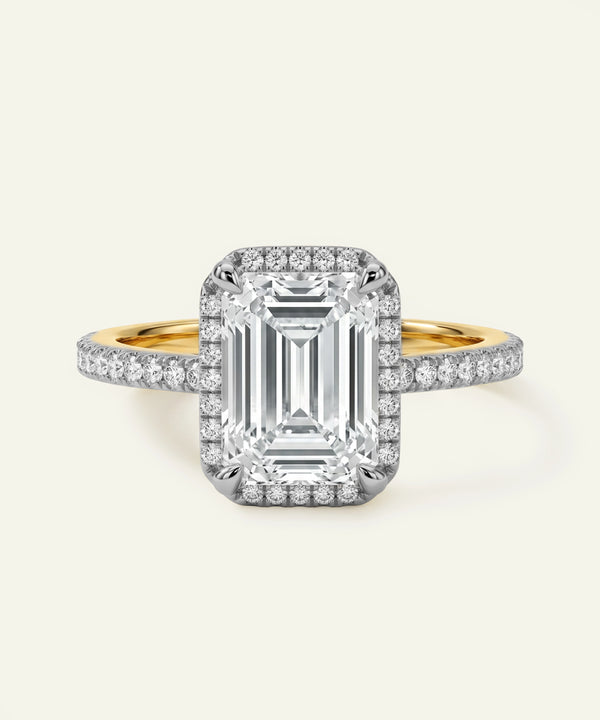 Diamond ring with emerald-cut center stone and gold band on a white background