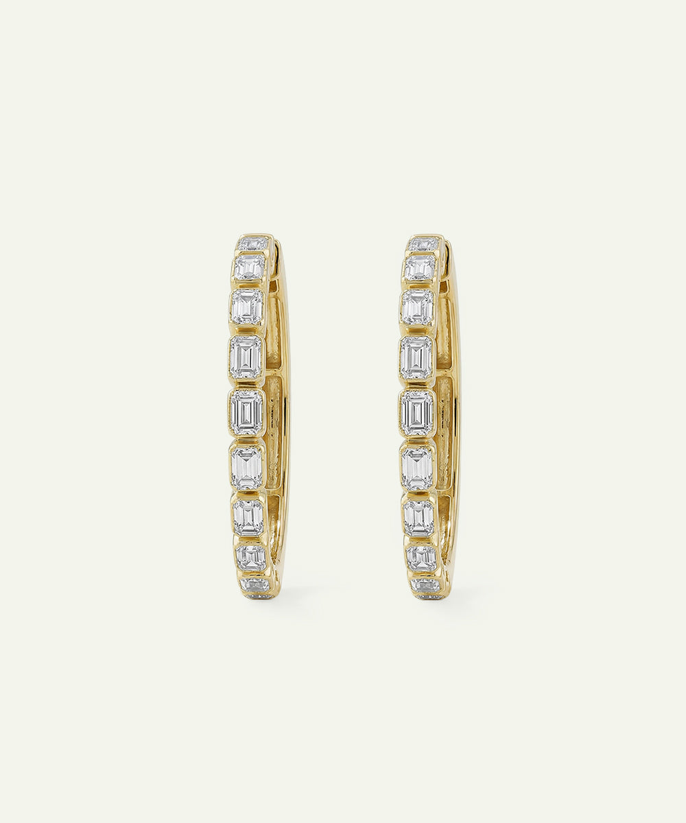 Gold hoop earrings with diamond accents on a light beige background
