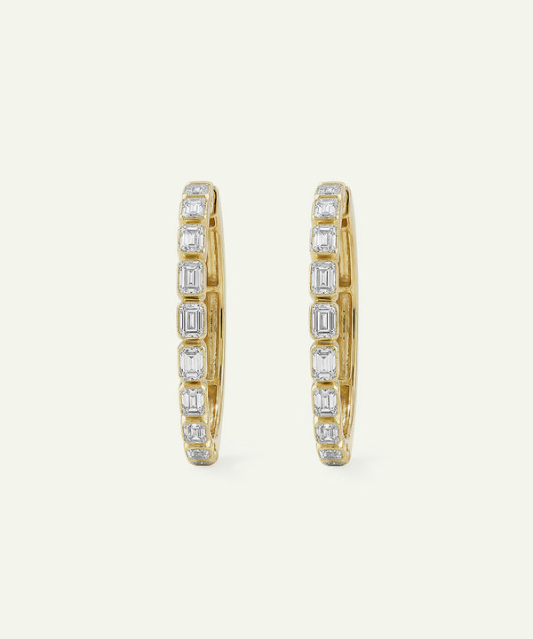 Gold hoop earrings with diamond accents on a light beige background