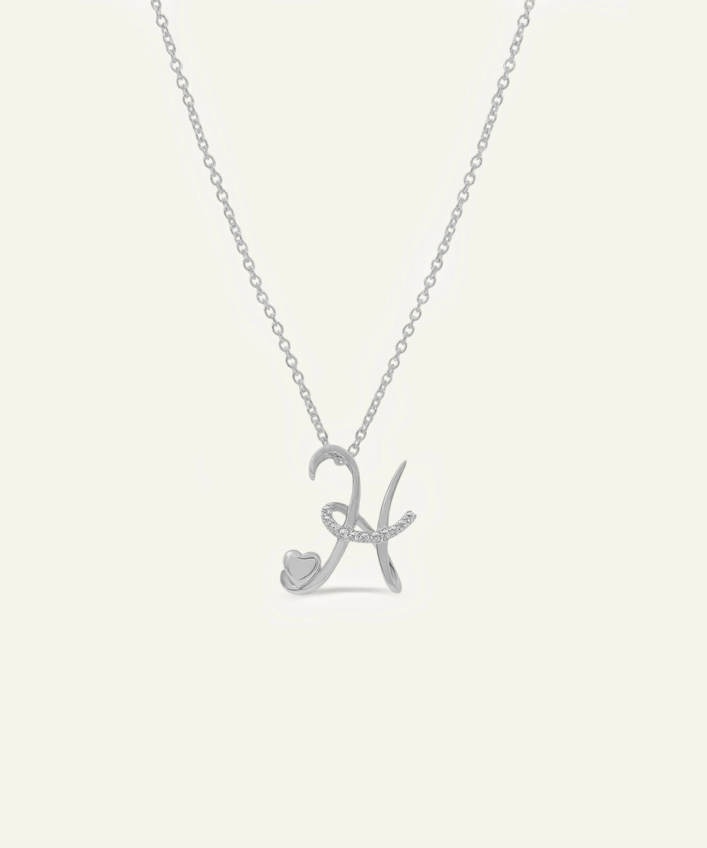 Silver necklace with a heart and letter 'K' pendant on a light gray background