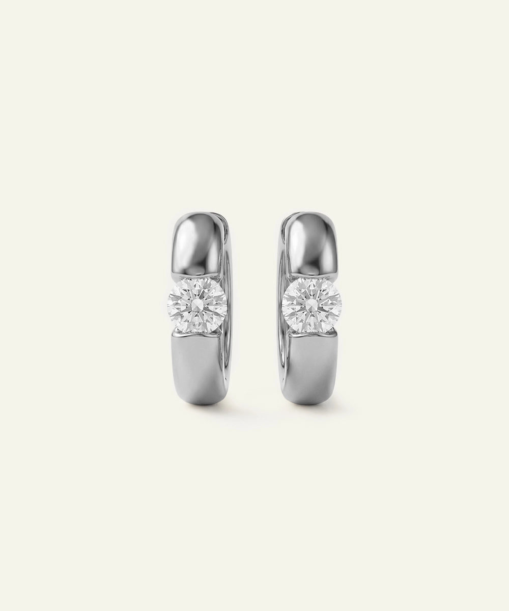 Pair of silver hoop earrings with clear gemstones on a light gray background