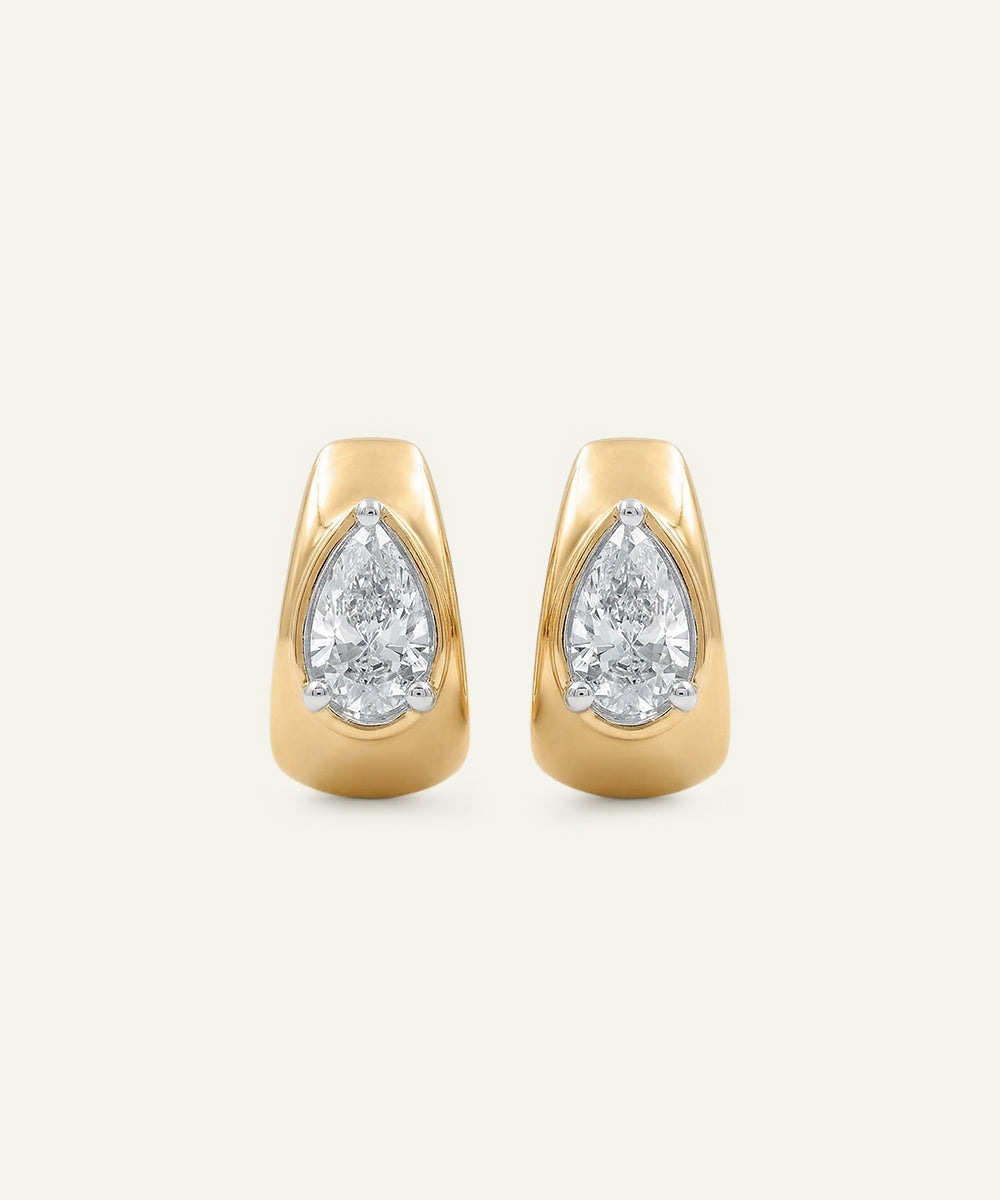 Gold earrings with pear-shaped diamond stones on a light beige background