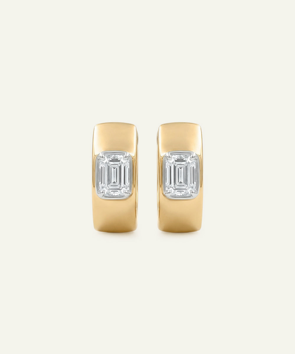 Pair of gold hoop earrings with emerald-cut gemstones on a light beige background