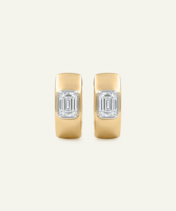 Pair of gold hoop earrings with emerald-cut gemstones on a light beige background