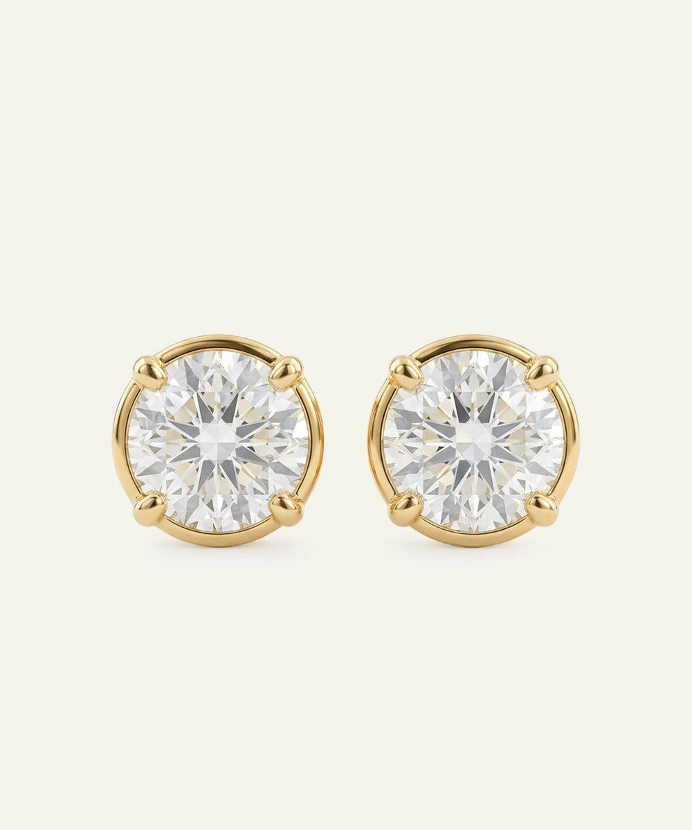Pair of gold stud earrings with clear gemstones on a beige background