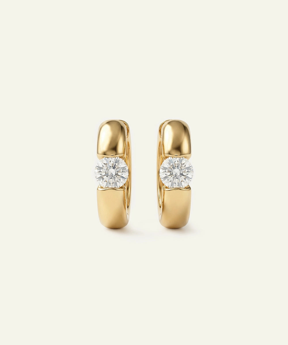 Gold hoop earrings with diamond-like stones on a light beige background