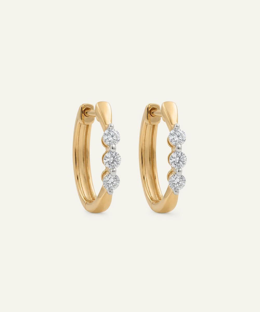 Gold hoop earrings with diamond accents on a light beige background