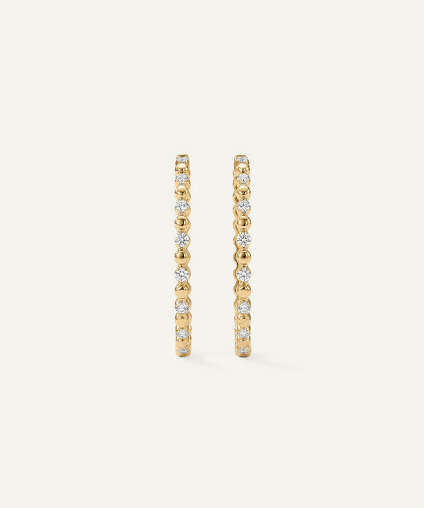 Gold hoop earrings with embedded diamonds on a beige background