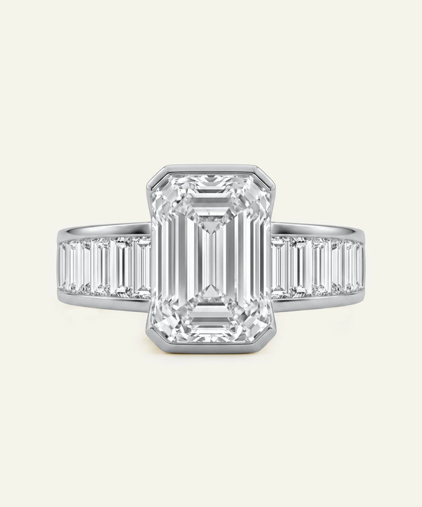 Diamond ring with emerald-cut center stone and baguette side stones on a light gray background