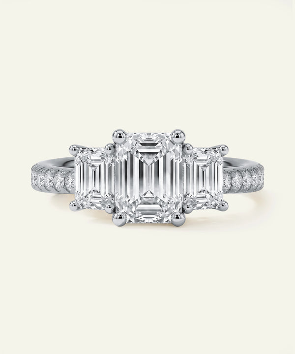 Diamond ring with emerald-cut center stone and smaller diamonds on a light grey background