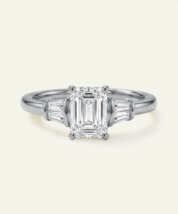 Diamond ring with emerald-cut center stone and baguette side stones on a light gray background