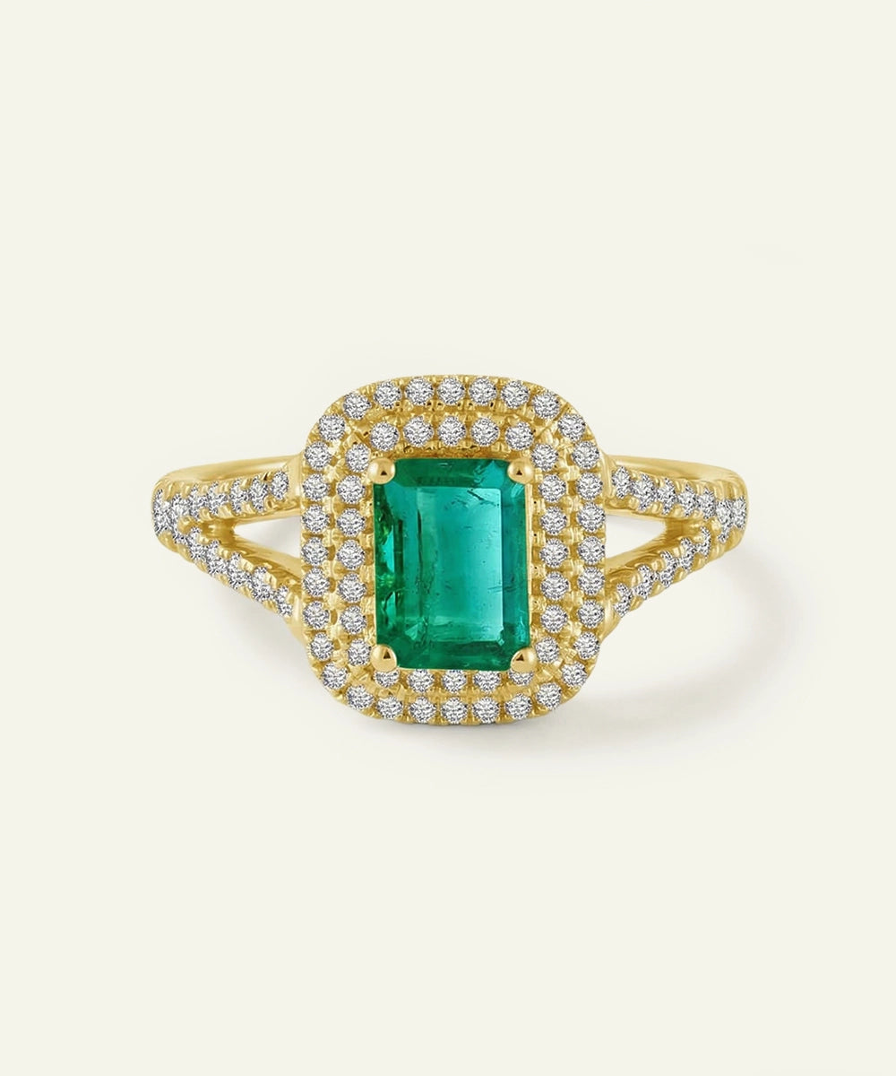 Gold ring with a green gemstone and diamond accents on a light beige background
