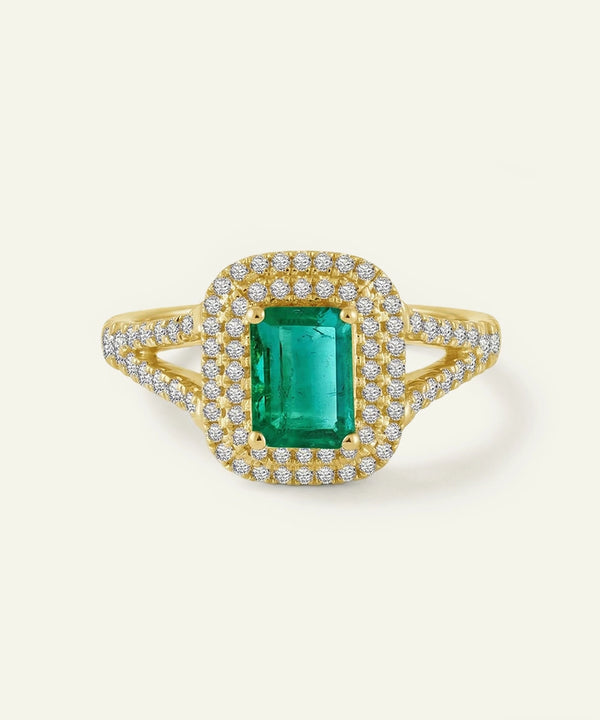 Gold ring with a green gemstone and diamond accents on a light beige background
