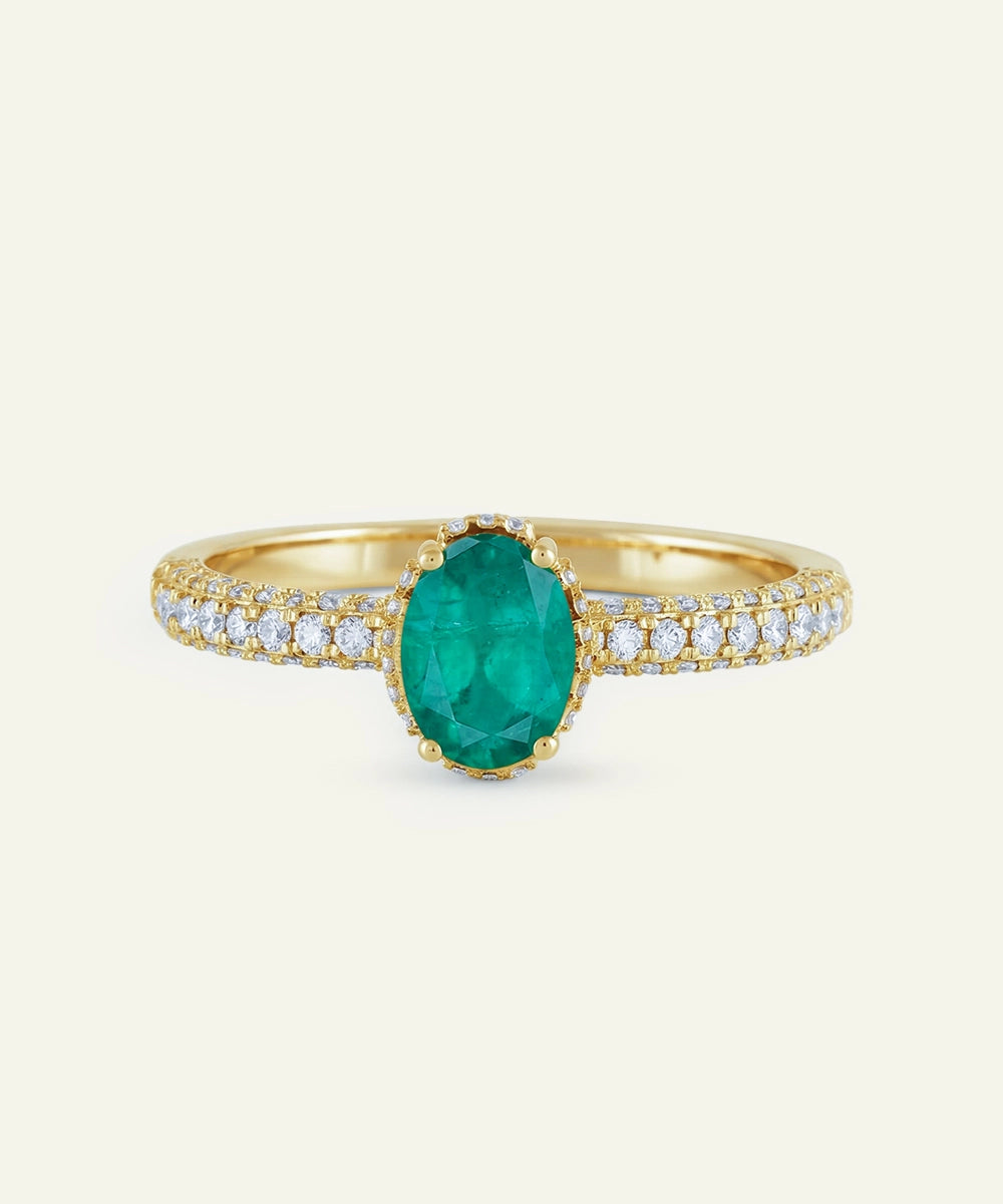 Gold ring with a green gemstone and diamond accents on a light beige background