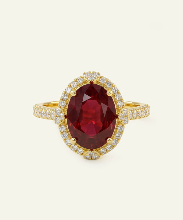 Gold ring with a red gemstone and diamond accents on a white background