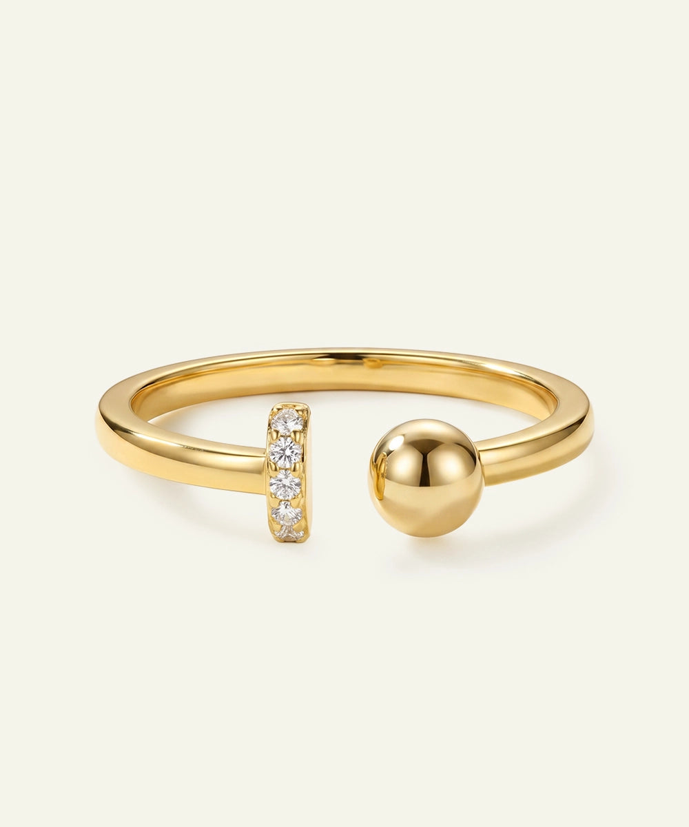 Gold ring with a spherical design and small diamond accents on a light beige background