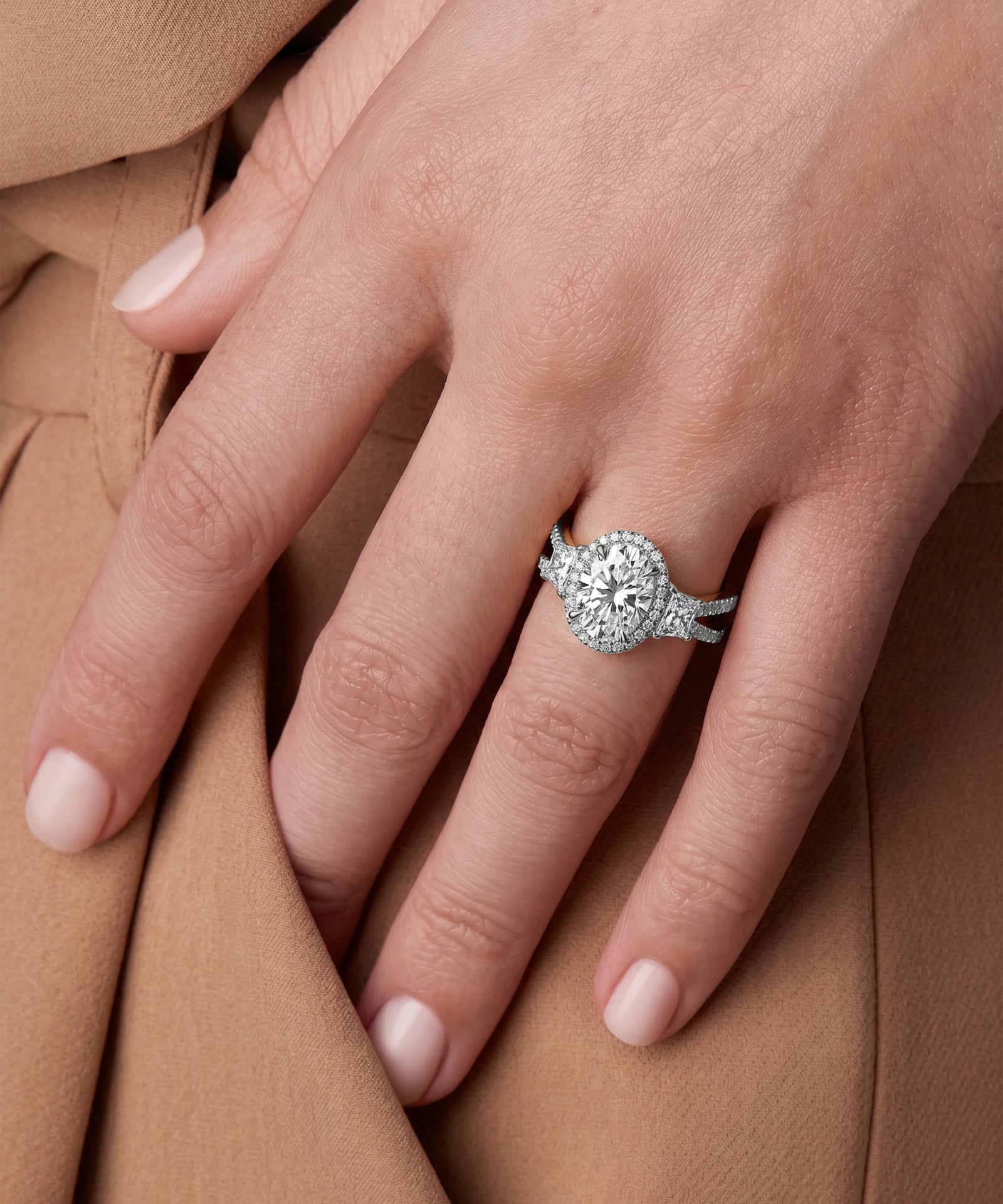 Close-up of a hand wearing a diamond ring on a brown fabric background