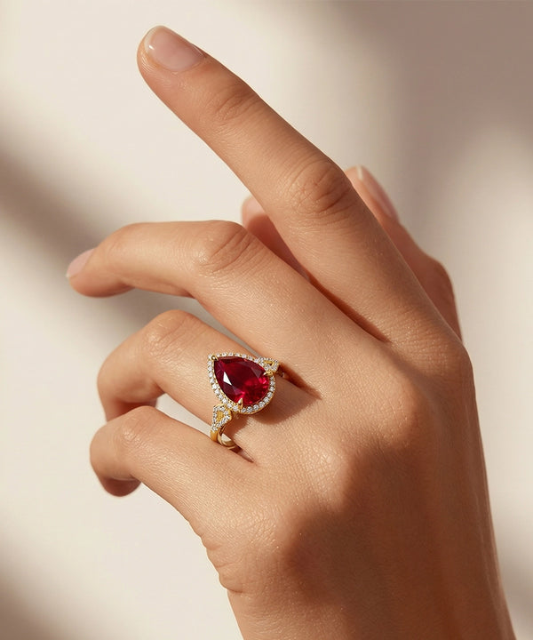 Hand wearing a ring with a red gemstone on a neutral background