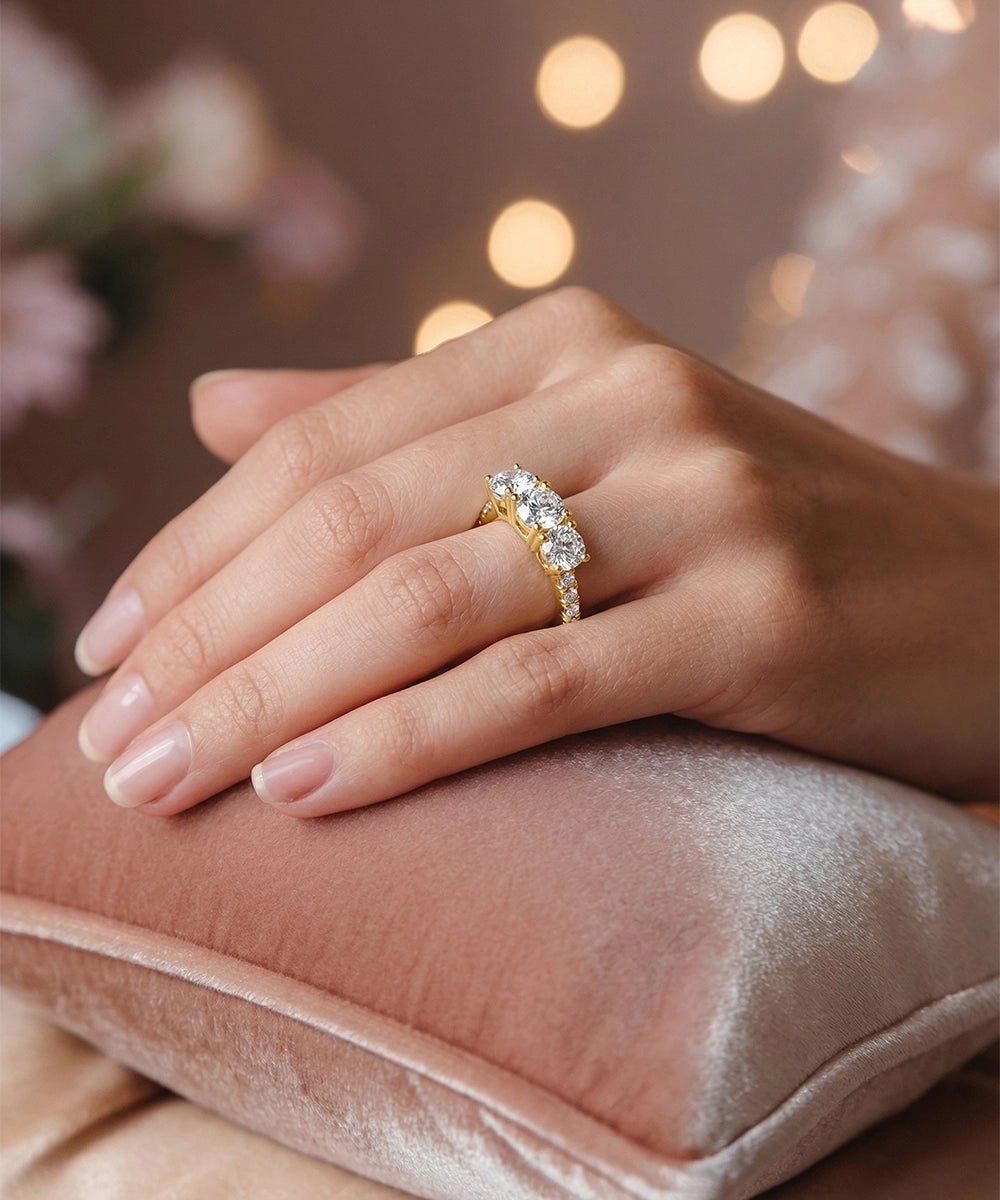 Hand wearing a gold ring with a diamond on a soft surface with blurred lights in the background