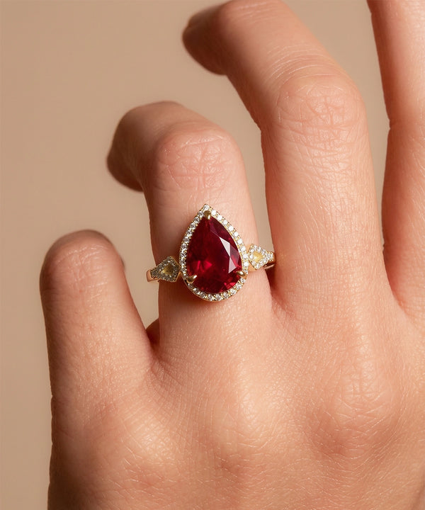 Gold ring with a red gemstone on a hand against a beige background