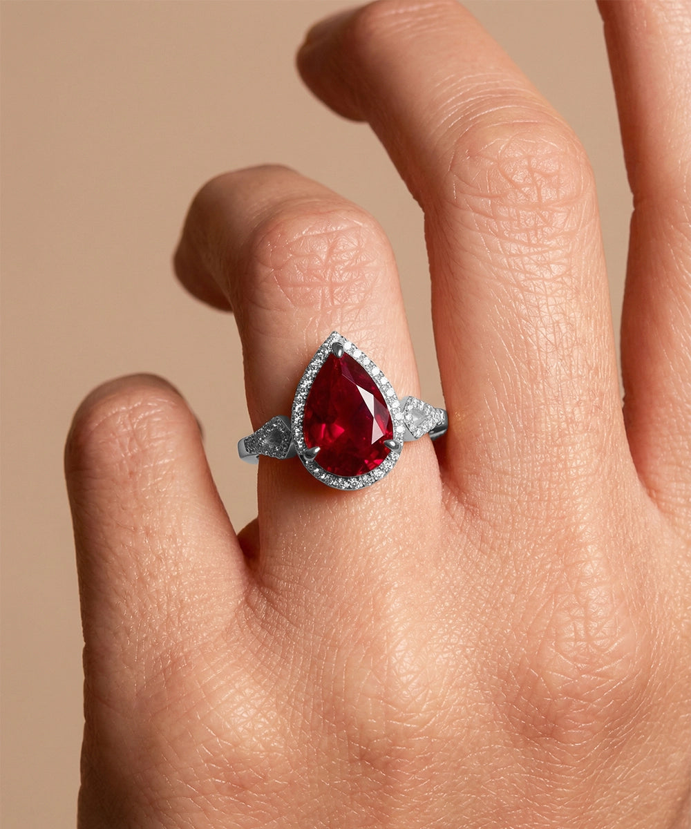 Gold ring with a red gemstone on a hand against a beige background