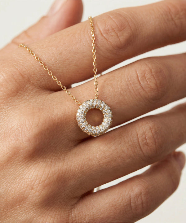 Gold necklace with a circular pendant on a hand against a neutral background