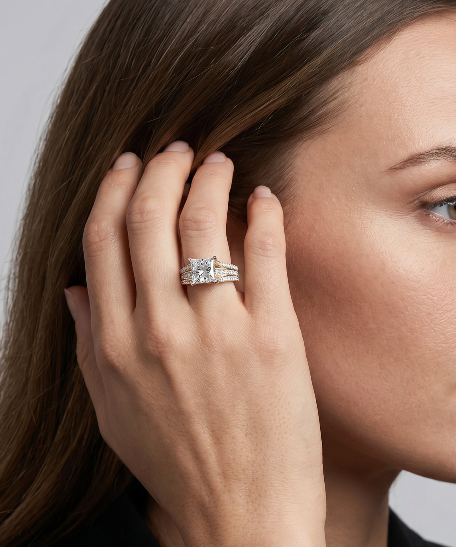 Close-up of a hand wearing a silver ring with a diamond, touching hair against a neutral background