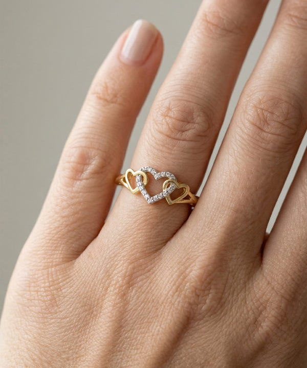 Gold ring with heart design on a hand against a neutral background