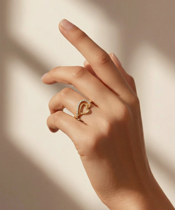 Hand wearing a gold heart-shaped ring with diamonds on a soft beige background