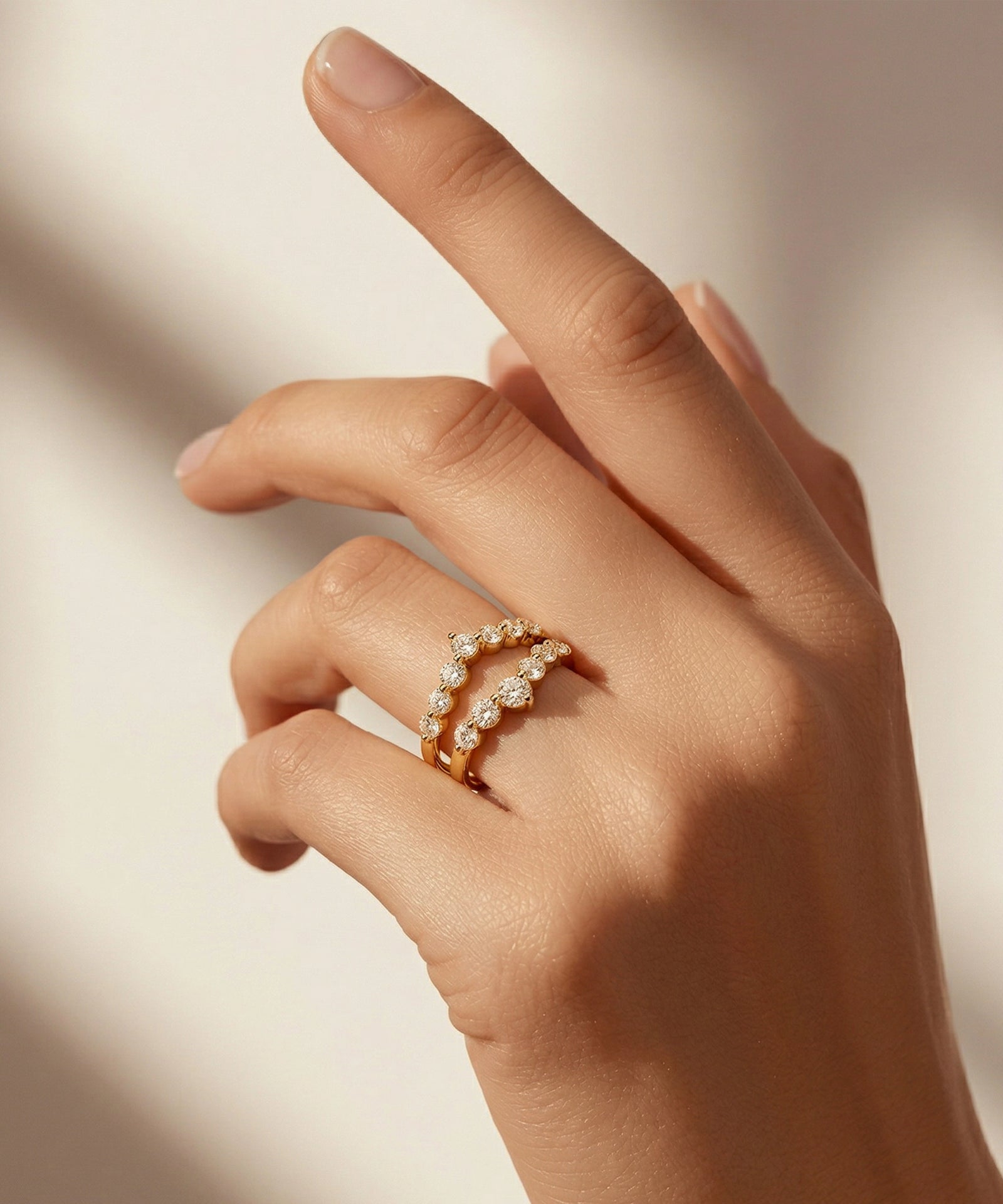 Hand wearing a gold ring with small diamonds on a neutral background